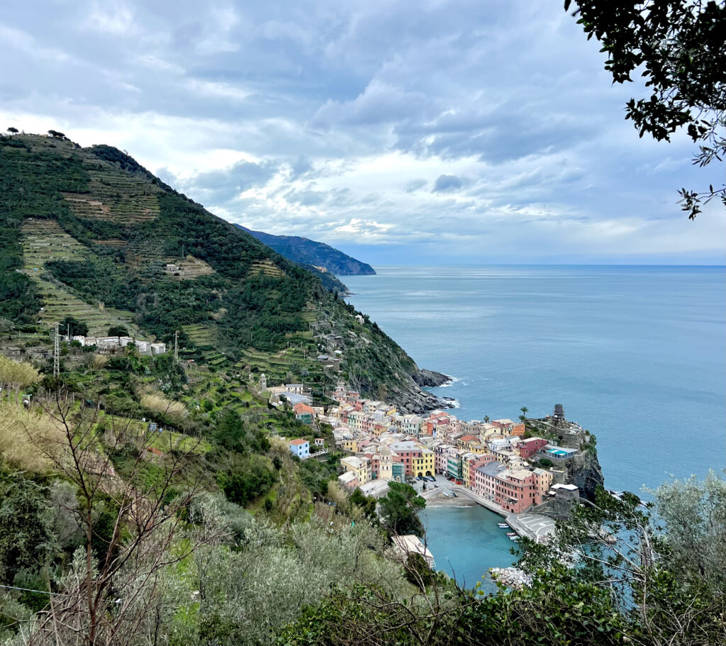 View of Vernazza, Cinque Terre, Italy from a beautiful coastal hike. Pastel buildings, vineyards, and the Mediterranean sea